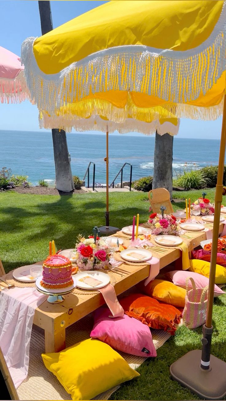 A beach picnic with a yellow fringed umbrella and pink florals overlooking the ocean
